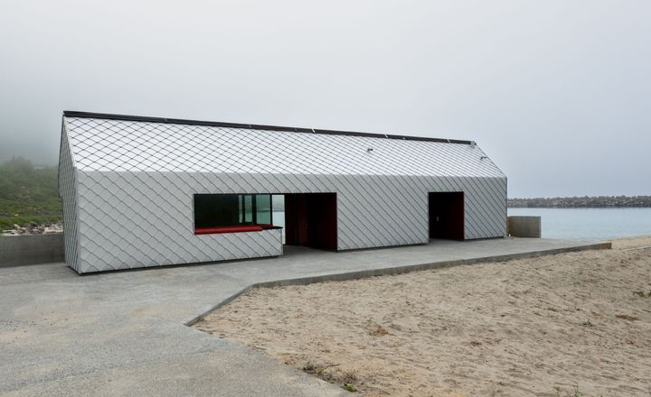 Et langstrakt servicebygg med sølvfarget kledning etablert i strandsonen ved Ersfjordstranda på Senja.