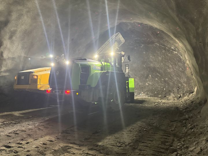 Bildet viser en hjullaster fremst i en tunnel under driving som laster sprengt stein opp i en dumper. Bildeteksten sier, Batteridrevet hjullaster under utlasting av sprengt stein i Rismålsheitunnelen på E6 Megården-Sommerset.