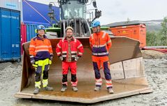 Bildet viser tre presoner med hjelm og verneutstyr som står fremme i skuffa til den batterielektriske hjullasteren på 40 tonn. Bildeteksten sier: Fornøyd gjeng: Fv. Stian Lauvluten, maskinformann i Skanska, prosjektleder Alf-Tore Angelsen i Statens vegvesen og prosjektleder Bjarte Næss hos utførende entreprenør, Skanska Norge AS.