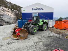 Bildet viser det batteridrevne hjullasteren til Skanska foran en anleggshall og batteriladeren. Bileteksten sier, Ruver: Det er store dimensjoner på en 40 tonns batteridrevet hjullaster. Ladestasjonen til høyre i bildet skal også byttes til en større type når storebroren på 60 tonn blir levert.