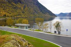 Oversiktsbilete av rasteplassen på Røyrnes. Eit toalettbygg ligg mellom vegen og fjorden, omgjeve av sitjeplassar, tre og bratte fjellsider med haustfargar.