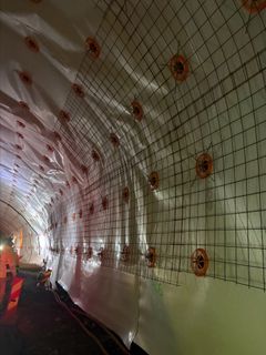 Bildet viser ferdig montert vanntett duk og påbegynt montering av armeringsnett utenpå duken. Bildeteksten sier, Armering og betong: Før betongen kan sprøytes på duken må det monteres heldekkende armeringsnett i tunnelens tak og vegger.