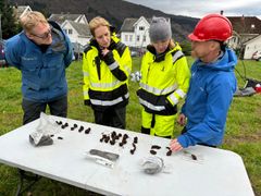 Bilde som viser noen av de mange hundre skipsnaglene som ble funnet i Myklebusthaugen liggende på et bord. Rundt bordet står fra venstre: Arkeolog Morten Ramstad, riksantikvar Hanna Geiran, UiB-rektor Margareth Hagen og  arkeolog Thomas Bruen Olsen.