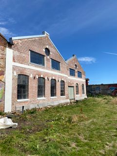 Renovert gavlvegg på gammel fabrikkbygning, med grønt gress i forgrunnen og blå himmel i bakgrunnen.