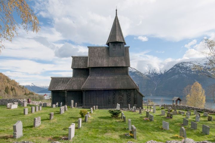 Bilde av Urnes stavkirke med fjell og fjord i bakgrunnen, og kirkegård i forgrunnen.