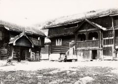 To tradisjonelle trebygninger med gresskledde tak; en person står ved inngangen til den venstre bygningen.