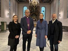 Fire voksne står side om side inne i en kirke med glassmalerier og et alter i bakgrunnen.