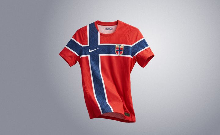En rød Nike-sportstrøye med det norske flagget og et våpenskjold på brystet, mot en grå bakgrunn.