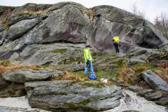 To personer iført refleksvester undersøker en stor fjellknaus; den ene står ved foten, mens den andre klatrer opp i fjellveggen.