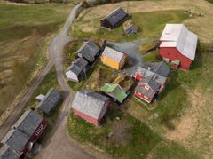 Flyfoto av en landsby med flere røde og gule hus, låver og uthus omgitt av gressletter og grusveier.