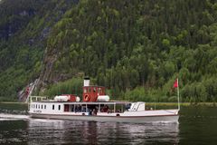 D/S Bjoren, en hvit passasjerbåt, med mennesker om bord beveger seg på en Byglandsfjorden, omgitt av tett, grønn skog og bratte åser.
