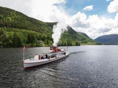 D/S Bjoren, en dampdrevet båt med hvit røyk stiger opp fra skorsteinen mens den beveger seg over Byglandsfjorden.