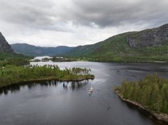 D/S Bjoren seiler på Byglandsfjorden omgitt av grønne skoger og åser under en overskyet himmel.