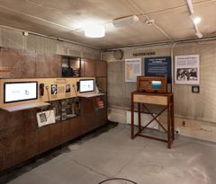 En utstilling på museet om media i krigstid, med interaktive skjermer, informasjonstavler og en gammel treradio på et stativ.