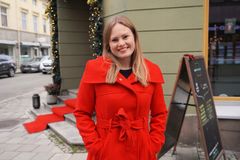 Kvinne med julerød kåpe og halvlangt hår i julepyntet bybilde smiler mot kameraet.