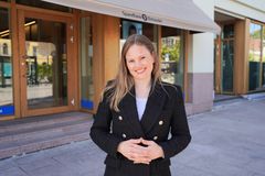 Portrettbilde av smilende kvinne med langt hår og svart blazer som står foran et banklokale.