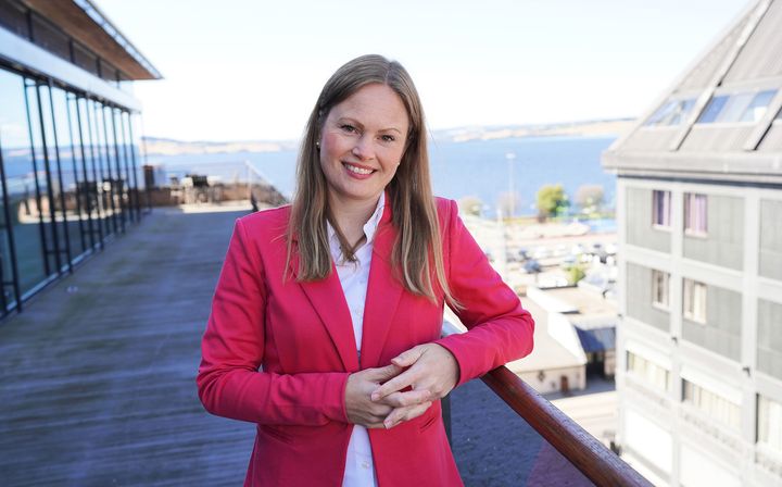 Portrett av blid kvinne med langt hår i rød blazer på toppen av en takterasse.