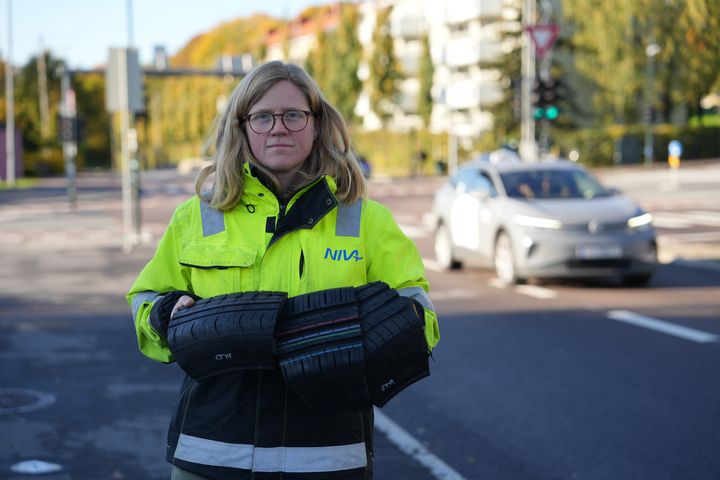 Kvinne holder deler av bildekk. Vei i bakgrunnen.