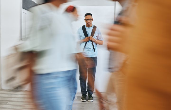 En trist mann går i gangen på et universitet omgitt av mange andre mennesker