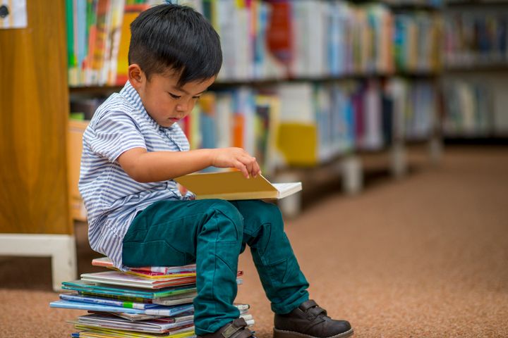 Liten gutt leser bok sittende på en bokstabel