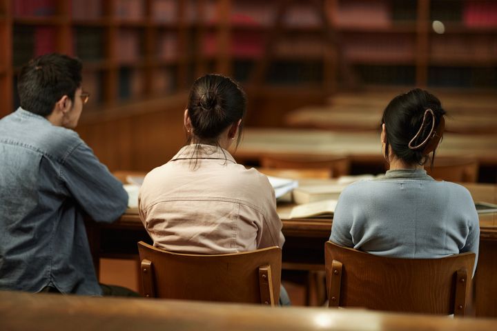 Tre studenter sitter sammen i biblioteket med ryggen til