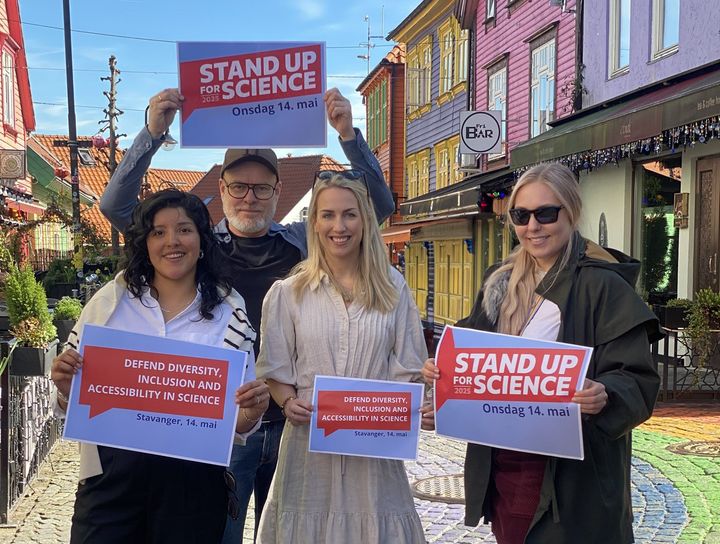 Fire smilende mennesker i Fargegata i Stavanger holder opp plakater med "Stand up for science"