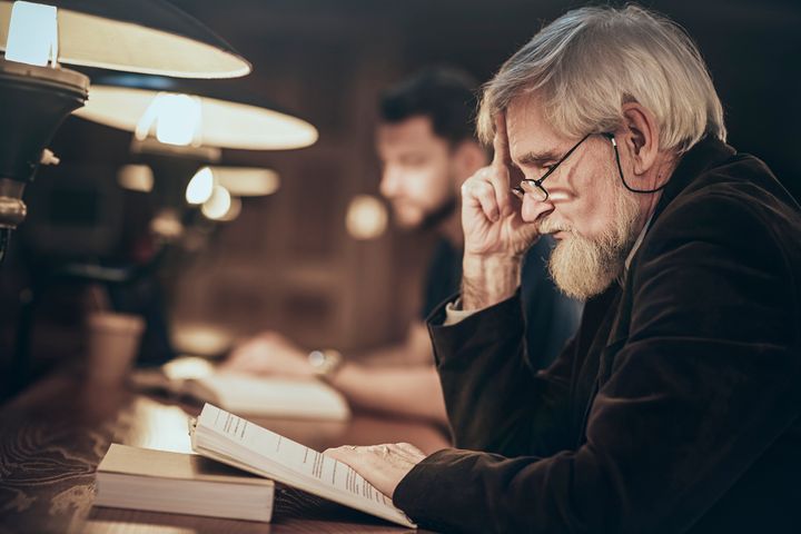 En eldre mann sitter og leser i en bok med flere lesende mennesker i bakgrunnen