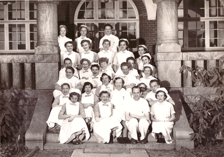 Historisk bilde av mange kvinnelige og sju mannlige ferdig utdannede sykepleiere i Danmark 1954, som sitter ute på en trapp