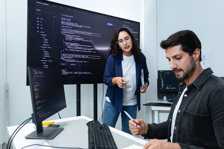 En kvinne og en mann står og diskuterer foran store pc-er