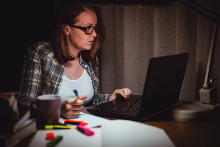 Ung, sliten kvinne jobber sent og sitter ved pc-en hjemmefra