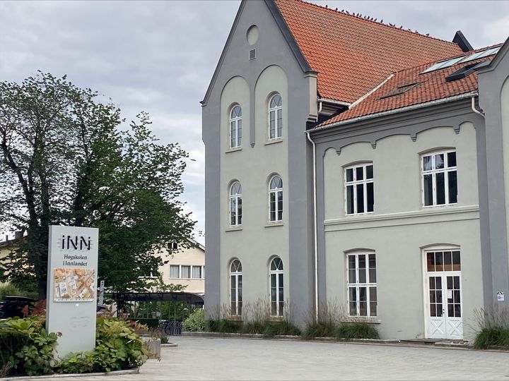 Skilt med høgskolen sin logo foran hovedbygget på studiestedet