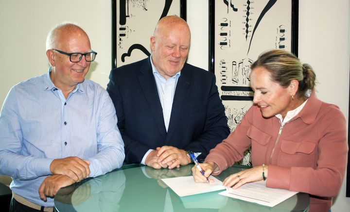 Per Atle Tufte, Peer Jacob Svenkerud og Anette Mellbye står ved et rundt bort mens Mellby signerer avtalen mellom partene.
