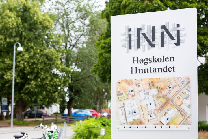 Et skilt med høgskolen i Innlandets logo, med trær i bakgrunnen
