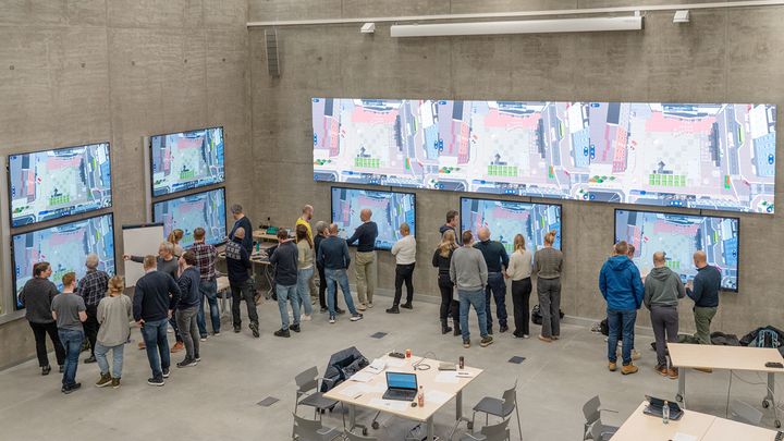 En gruppe mennesker samlet ved en vegg med mange skjermer