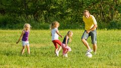 Mann spilelr fotball i en hage med tre barn