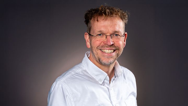 Mann i hvit skjorte mot mørk bakgrunn.