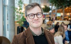 Mann med briller og brun jakke i ei kantine ser i kamera