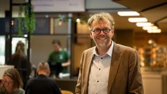 Mann med briller og brun dressjakke i et kontoprfellesskap