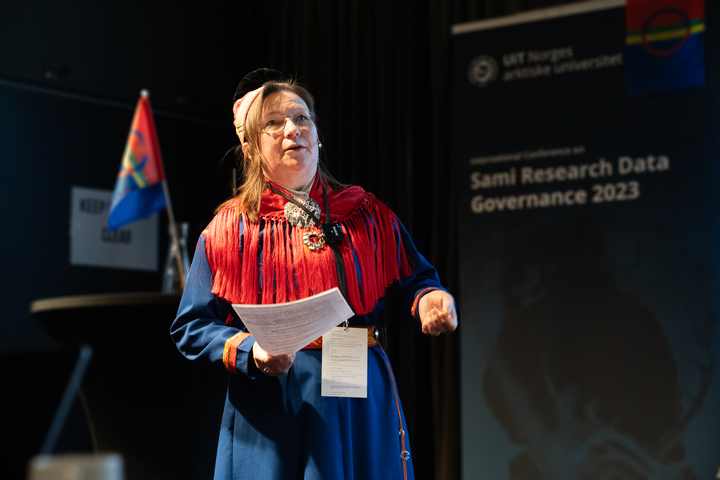 Kvinne i tradisjonelle samiske klær snakker på en scene.