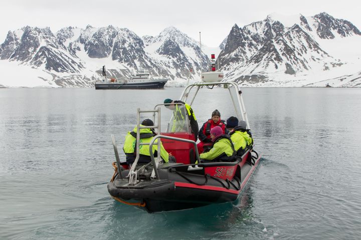 forskere som sitter i gummibåt med fjell med snø og is i bakgrunnen