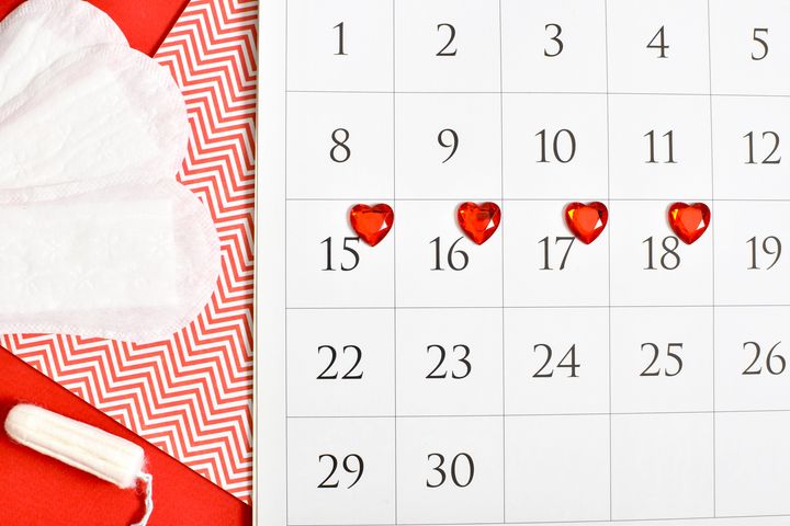 kalender med mensen markert med røde hjerter og bind og tamponger som ligger ved siden av