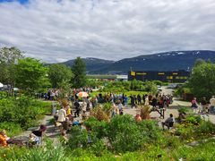 Bilde av en travel botanisk hage med mange mennesker, omgitt av grønne planter og fjell i bakgrunnen.