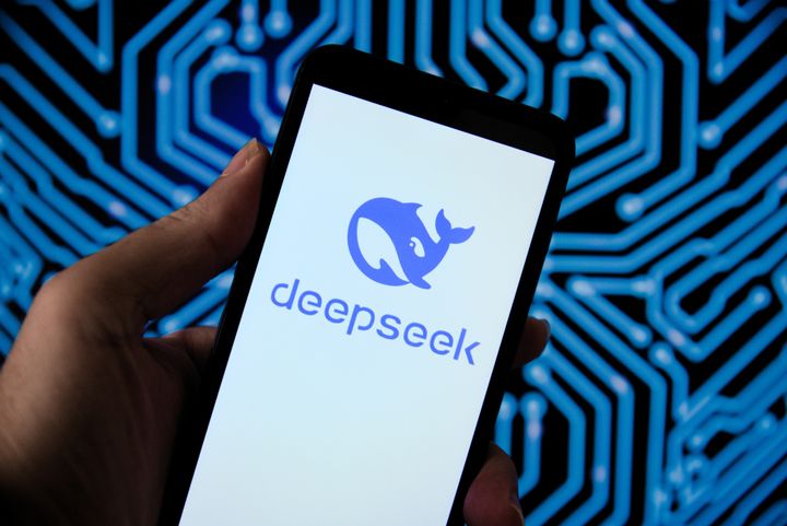 En hånd holder en mobiltelefon som viser en blå logo av en hval med teksten "deepseek" på en bakgrunn med et kretsmønster.