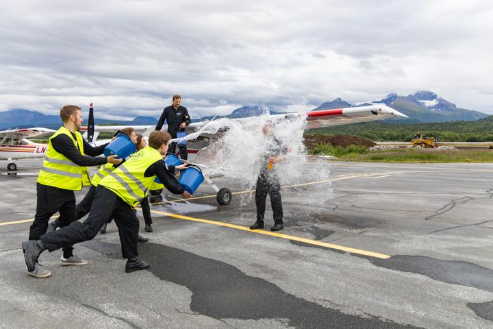 En gruppe mennesker heller vann på en person foran et småfly på en flyplass.