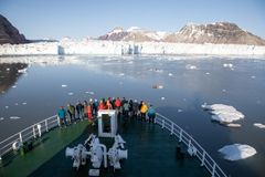 En gruppe mennesker står på dekk av FF Helmer Hanssen og ser mot en isbre på Svalbard.