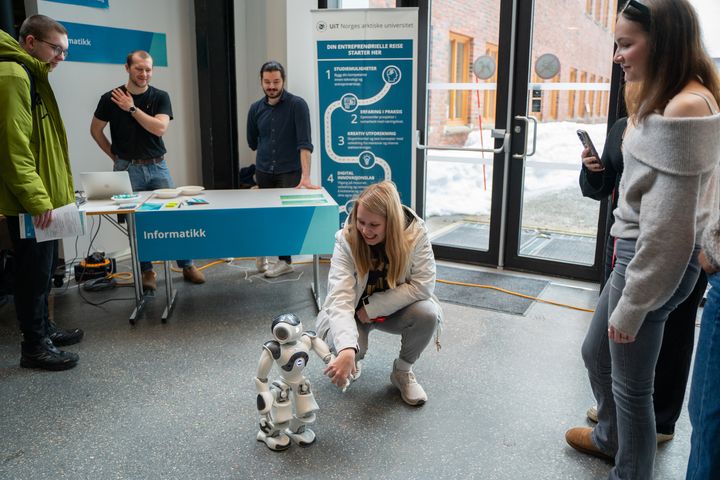 Ei jente sitter på huk og hilser på en liten robot på gulvet