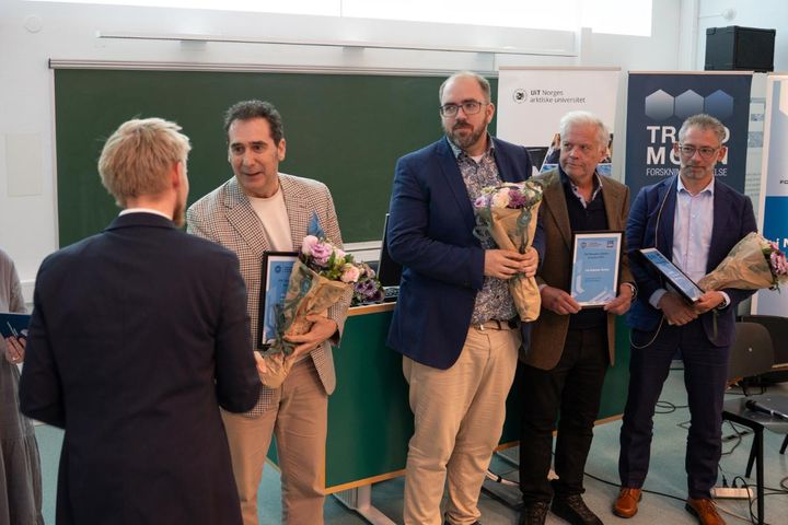 En gruppe menn som mottar priser under en seremoni, noen holder blomsterbuketter og diplomer.