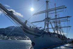 Et stort seilskip, SS Statsraad Lehmkuhl, ligger til kai i solfylt vær med fjellandskap i bakgrunnen.