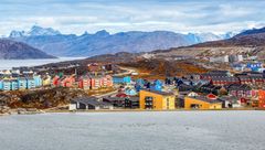 Panoramic view of colorful buildings in Nuuk, Greenland, with mountains in the background and water in the foreground.