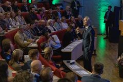 En mann taler foran et publikum på en konferanse i et auditorium.